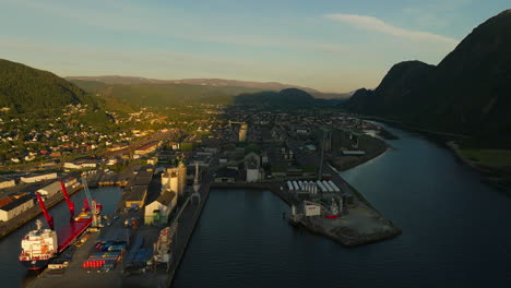 Cargo-vessel-moored-at-Mosjoen-Dock,-setting-sun-casts-shadows-over-city