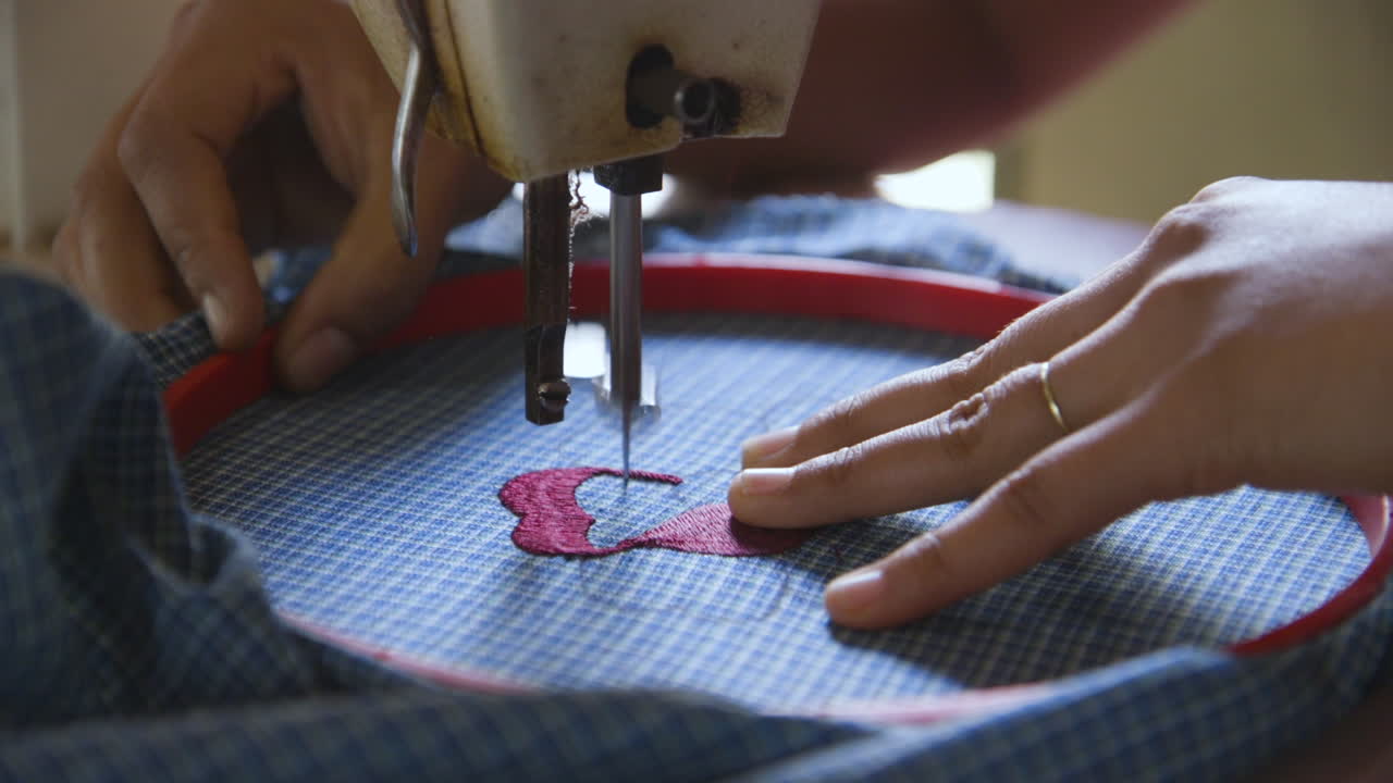 un primer plano de las manos de una mujer mientras trabaja en una máquina de coser para bordar un diseño floral en un delantal