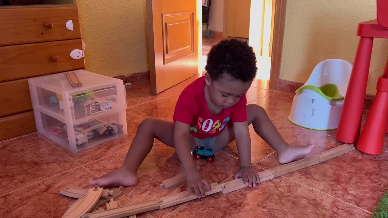 encantador niño negro de dos años que se une a las vías del tren para jugar con su tren de juguete en casa