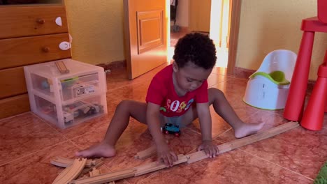 encantador niño negro de dos años que se une a las vías del tren para jugar con su tren de juguete en casa