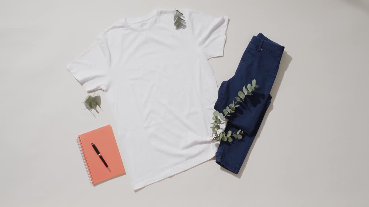 Video of flat lay of white t shirt, denim trousers, notebook and copy space on white background