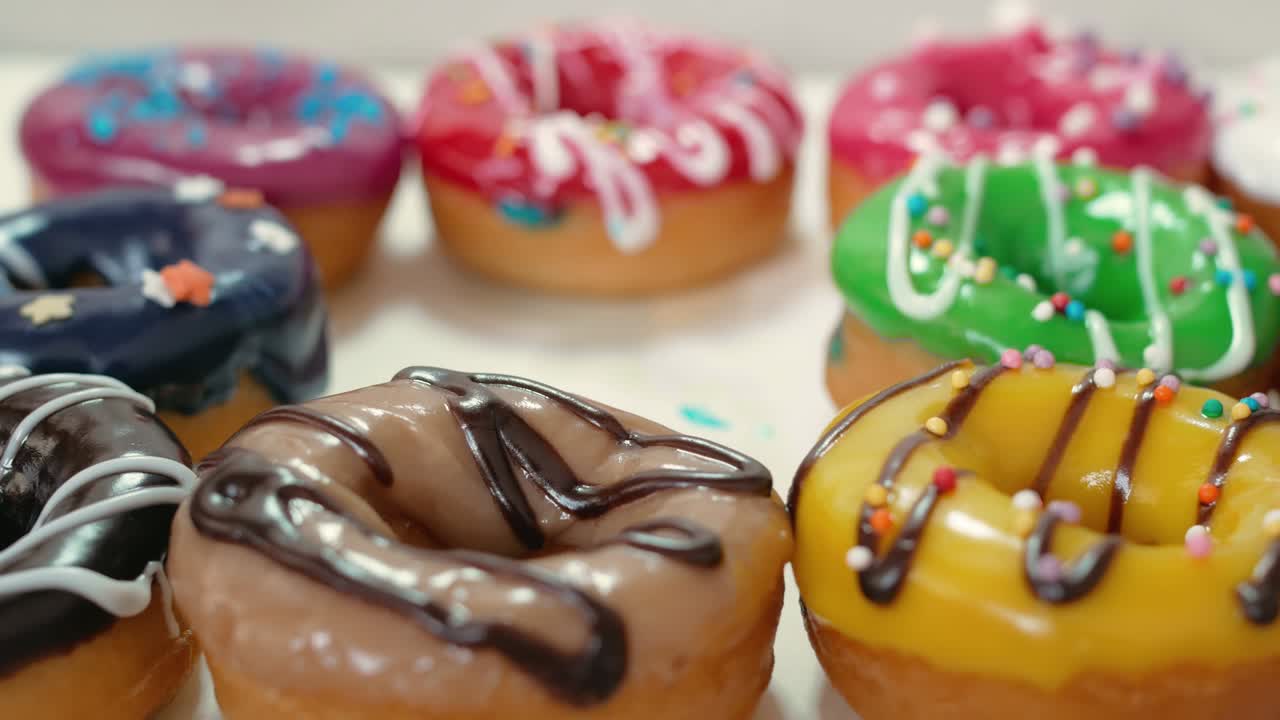 con dos dedos del pincel, tome una rosquilla con esmaltado azul. las rosquillas están bañadas con esmaltes de frutas de diferentes colores y chocolate blanco oscuro. dulces de primer plano. comida chatarra