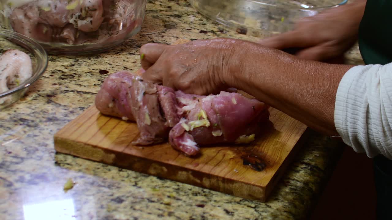 Close-up tangan wanita tua memotong daging babi mentah di atas talenan, bahan-bahan segar, memasak di dapur rumah, persiapan kuliner tradisional