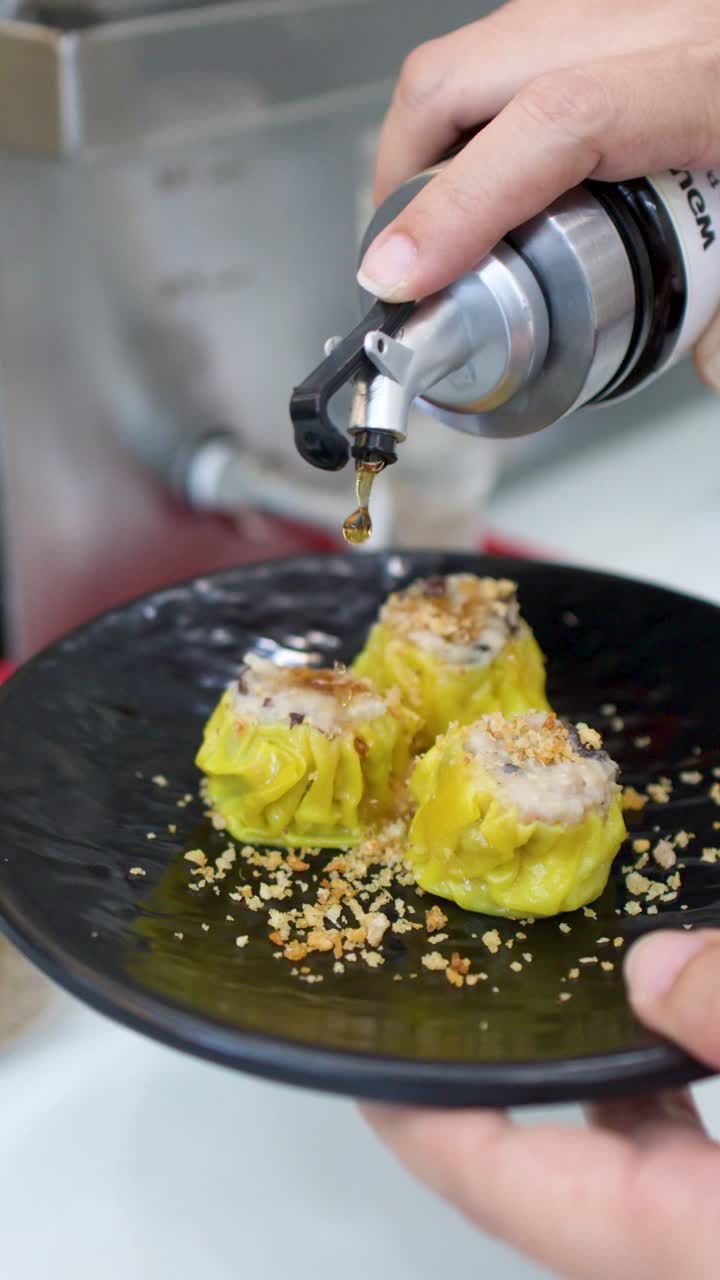Una persona versa salsa scura da un dosatore su ravioli shumai gialli in un ristorante.