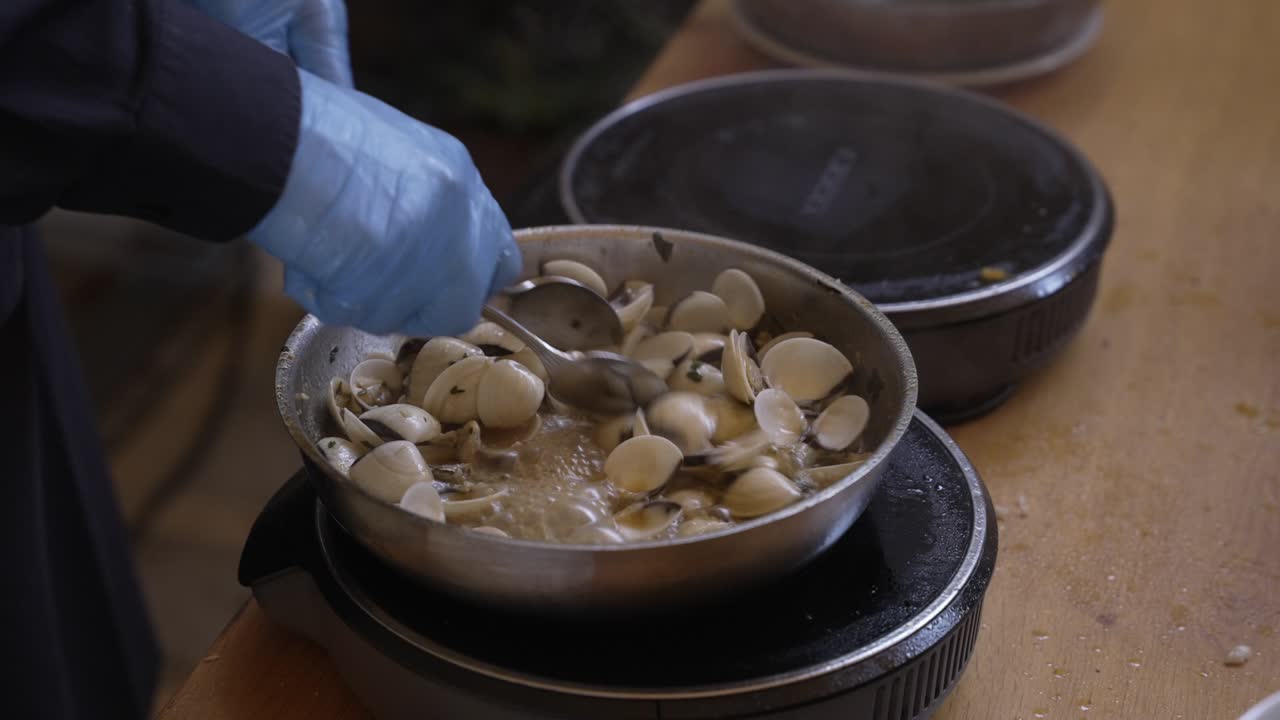 fresh clams cooked in pan with gloved hands on electric stove