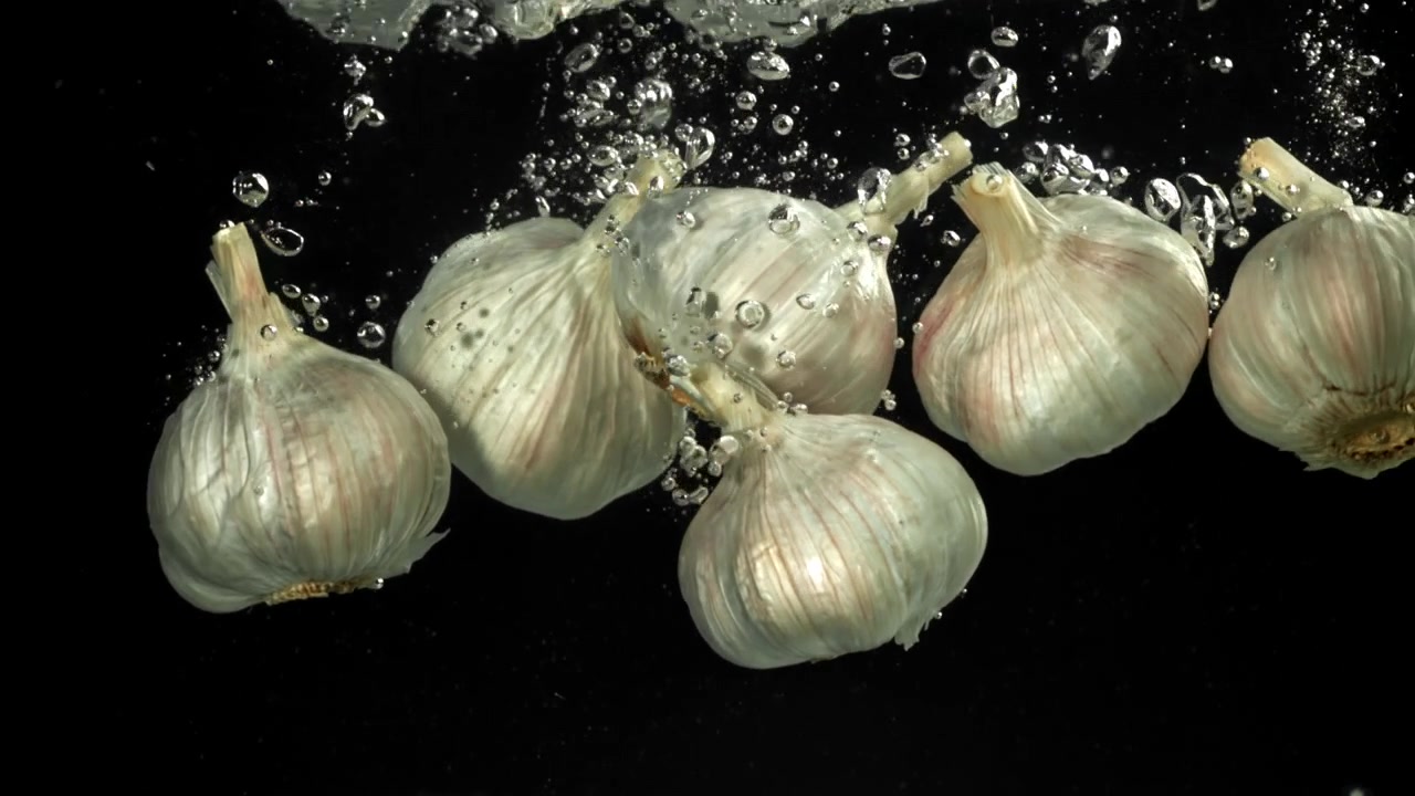 Bulbi d'aglio freschi che cadono nell'acqua al rallentatore