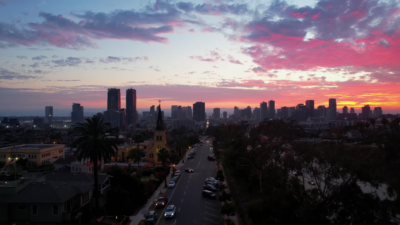 Dron ascendiendo hacia el horizonte del centro de San Diego a las 8 PM, con un cielo de atardecer vibrante en tonos rosa, morado y rojo, creando una atmósfera nocturna dramática.