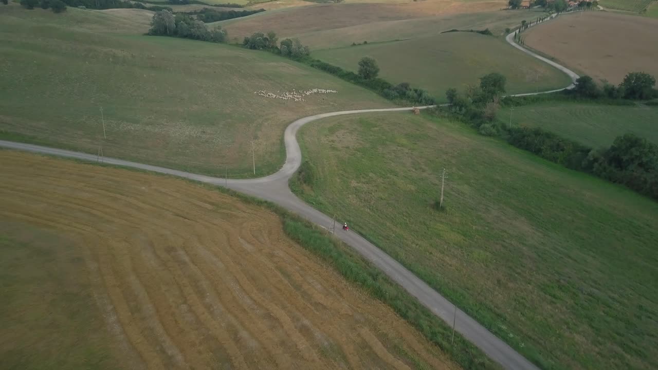 vista aérea de ciclismo en la carretera de retorno sobre las colinas con el campo de tierras agrícolas en la toscana, italia