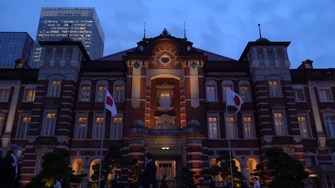 통근자들이 움직이는 밤의 유명한 도쿄역과 배경에 있는 고층 빌딩 - 낮은 각도의 좁은 시야