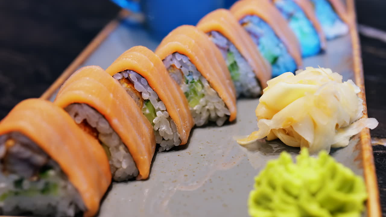 Close up of triangle shaped salmon sushi on a platter with wasabi and gari