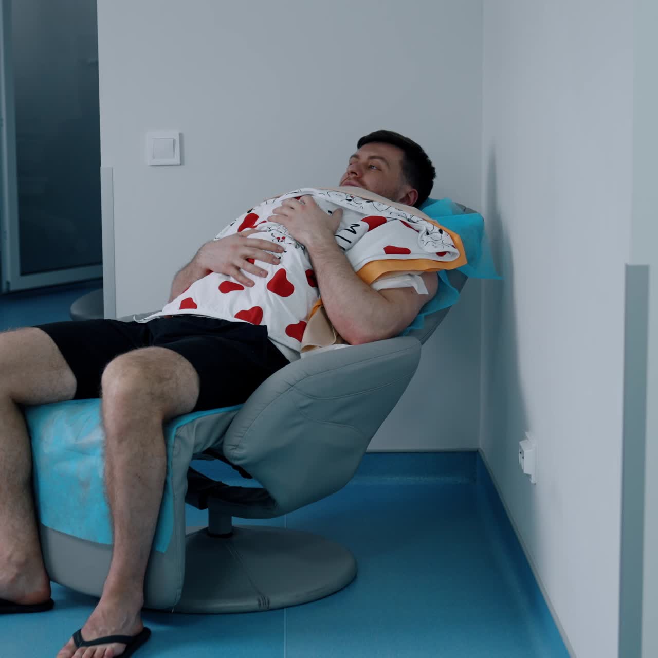 Caucasian man sits in a chair holding a newborn child on the chest. Loving dad taking care of his baby