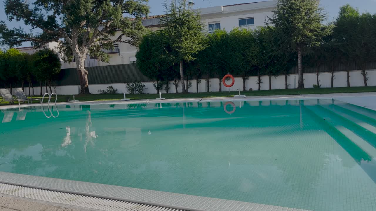 Smuk stor turkis udendørs swimmingpool med små fugle der flyver over vandet i solrige Portugal