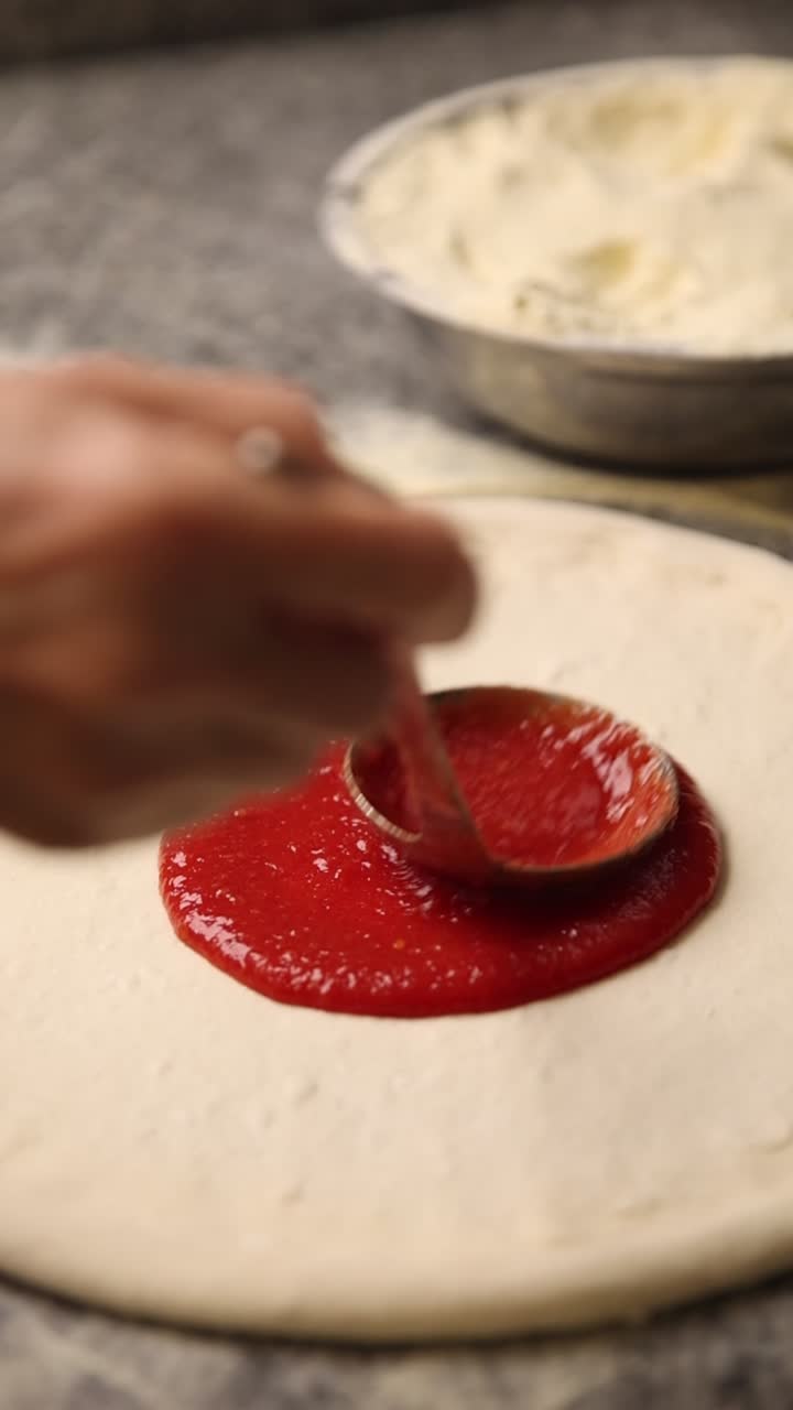 Spreading Tomato Sauce on Fresh Pizza Dough with a Spoon