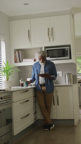 video vertical de un anciano afroamericano feliz bebiendo café y usando una tableta