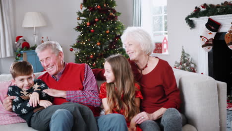 Retrato-De-Abuelos-Con-Nietos-Sentados-En-Un-Sofá-En-El-Salón-De-Casa-El-Día-De-Navidad