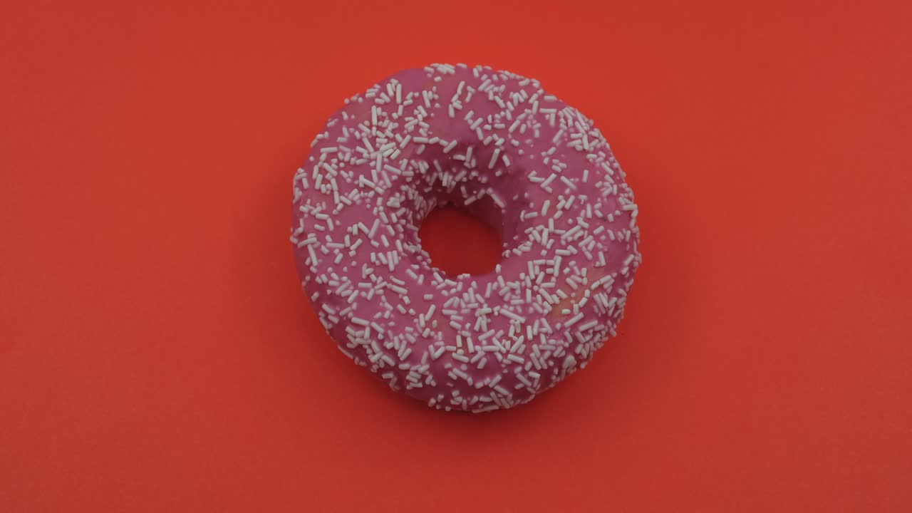 rotación de primer plano de rosas sabrosas deliciosas rosquillas dulces con salpicaduras coloridas en fondo rojo