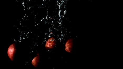 Plums-dropped-into-water-on-black-background,-slow-motion-close-up