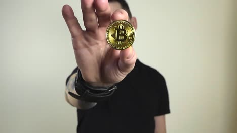 imágenes de un hombre sosteniendo una moneda de bitcoin reflectante de color amarillo dorado delante de él moviéndola lentamente. el movimiento crea nuevos reflejos. el hombre tiene tatuajes, cabello corto y barba