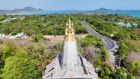 drone footage reveals promthep cape lighthouse amidst lush greenery and coastal views in phuket, thailand, under bright daylight