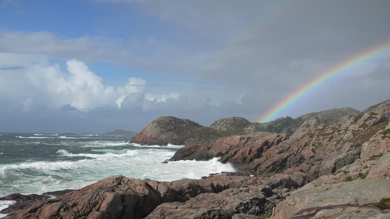 A vibrant rainbow stretches across the sky, creating a stunning contrast against rocky cliffs and patches of green moss under a dramatic sunset sky