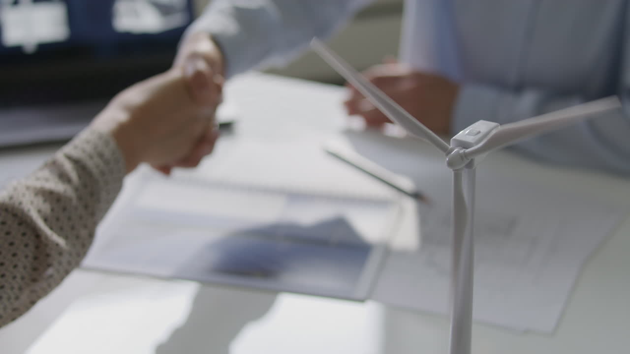 Close Up of Wind Turbine Model on Desk with Engineers Shaking Hands Behind