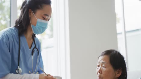 asian female nurse wearing face mask bringing soup to senior female patient sitting in hospital bed