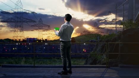 vista trasera completa del cuerpo de un trabajador profesional masculino asiático de pie con un teléfono inteligente de pantalla verde cerca de la torre de alto voltaje, instalación industrial