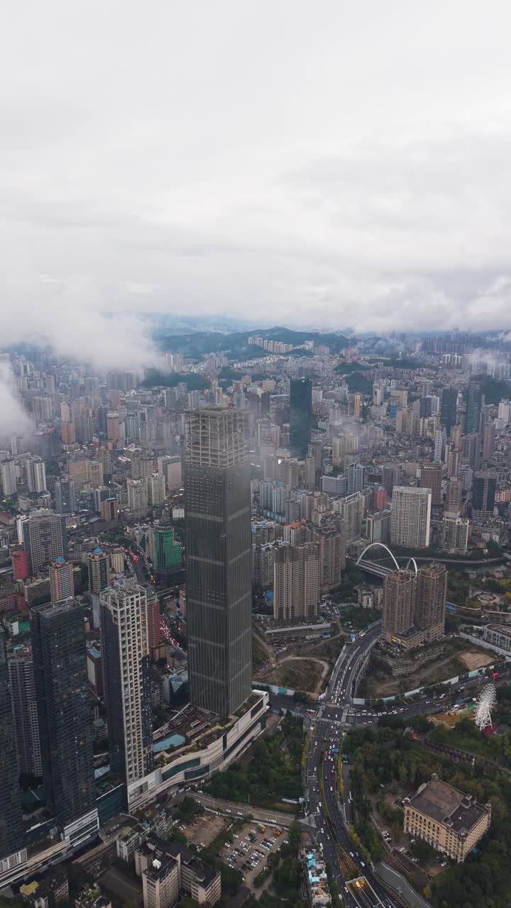 Vertical aerial of the massive Hengfeng Guiyang Center Tower 1 under construction, soaring above the dense, sprawling cityscape of Guiyang, China. Urban growth and development