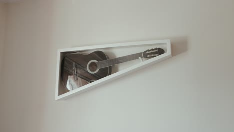 vintage wooden guitar encased in angled frame on clean modern wall