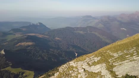 a hiker stands on the edge of a mountain ridge and puts is hands in the air