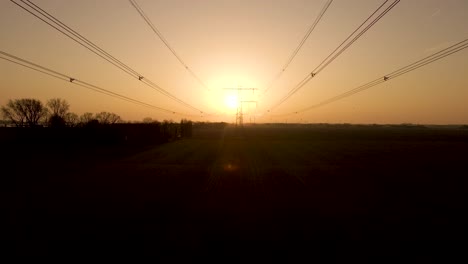 Retroceso-Aéreo-A-Lo-Largo-De-Líneas-Eléctricas,-Silueta-De-Torre-Eléctrica-Durante-La-Puesta-De-Sol