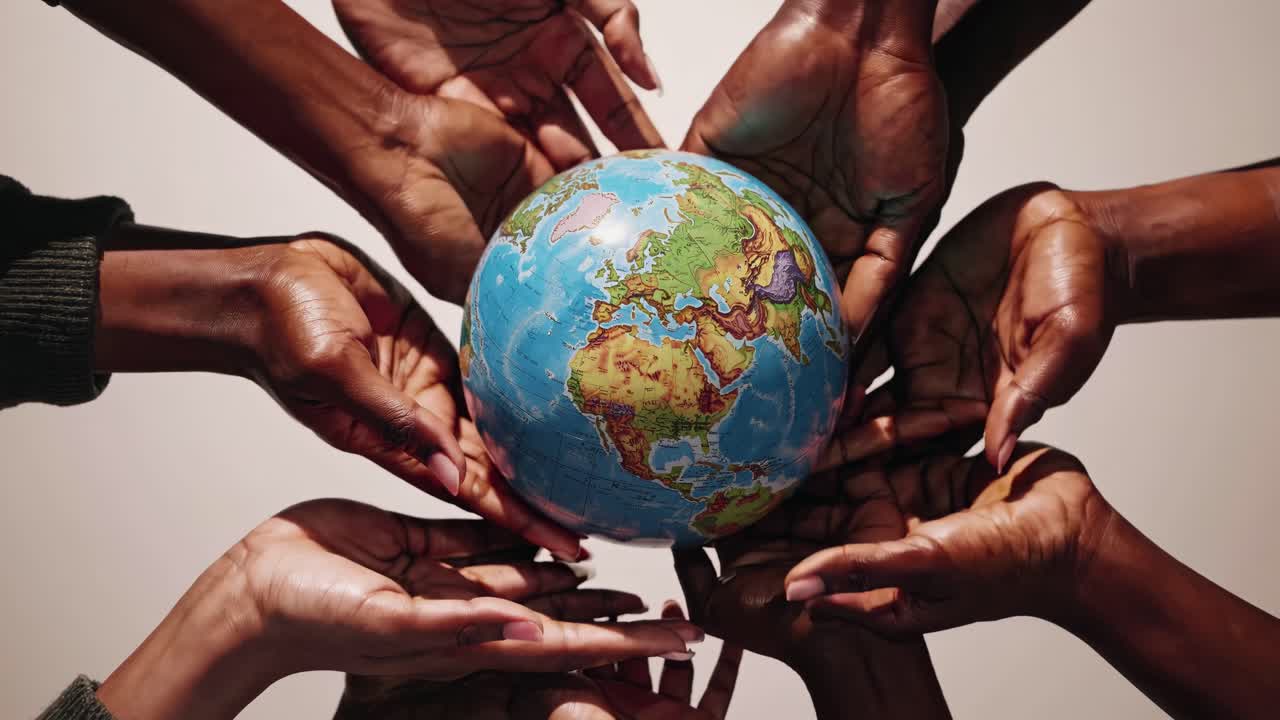 A diverse group of hands holding a globe, shot from a top-down angle