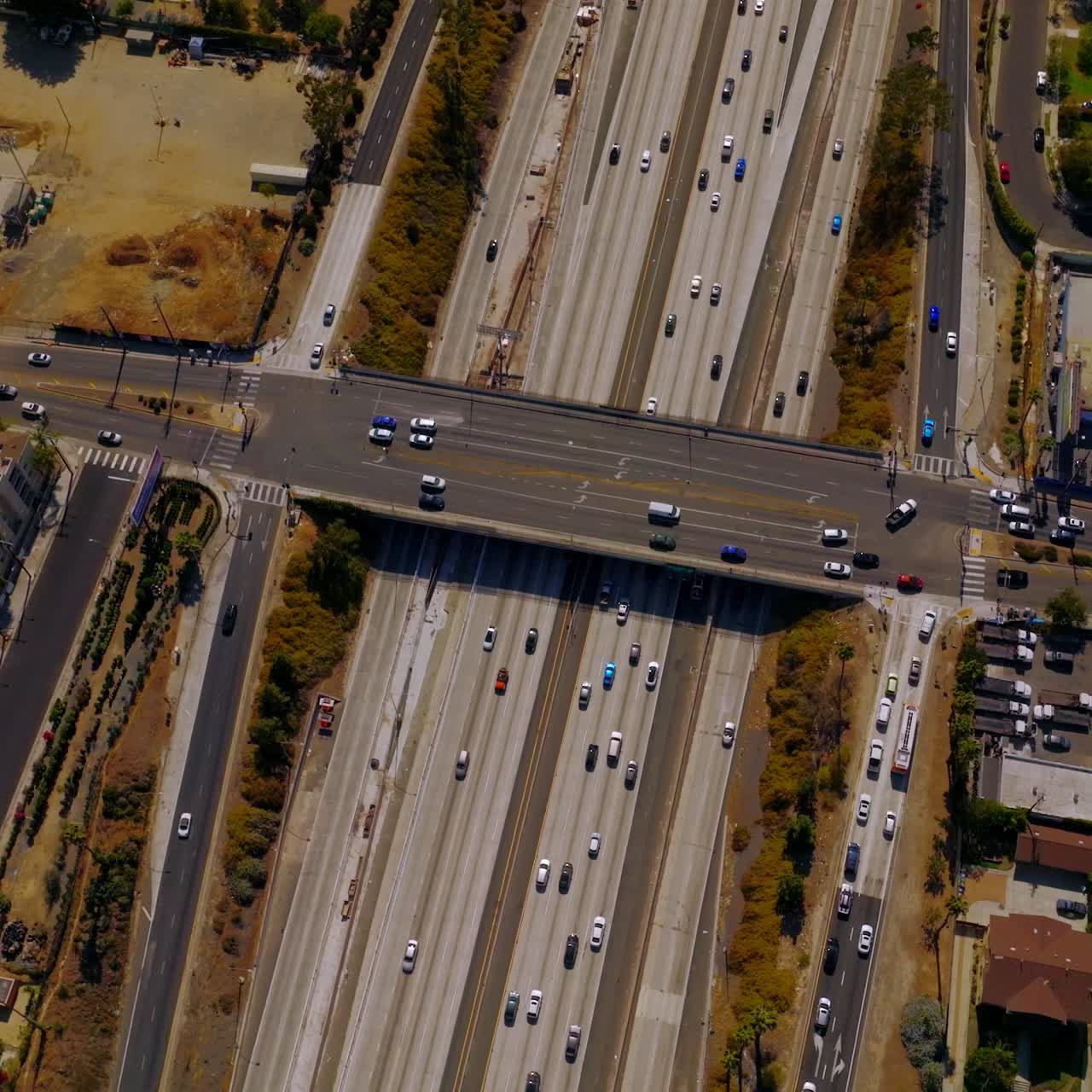 Road bridge over the wide multi-lane motorway with busy traffic. Drone descending over the freeway in Los Angeles, California, USA on sunny hot day