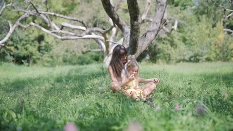 mother and daughter sitting in a meadow under a tree