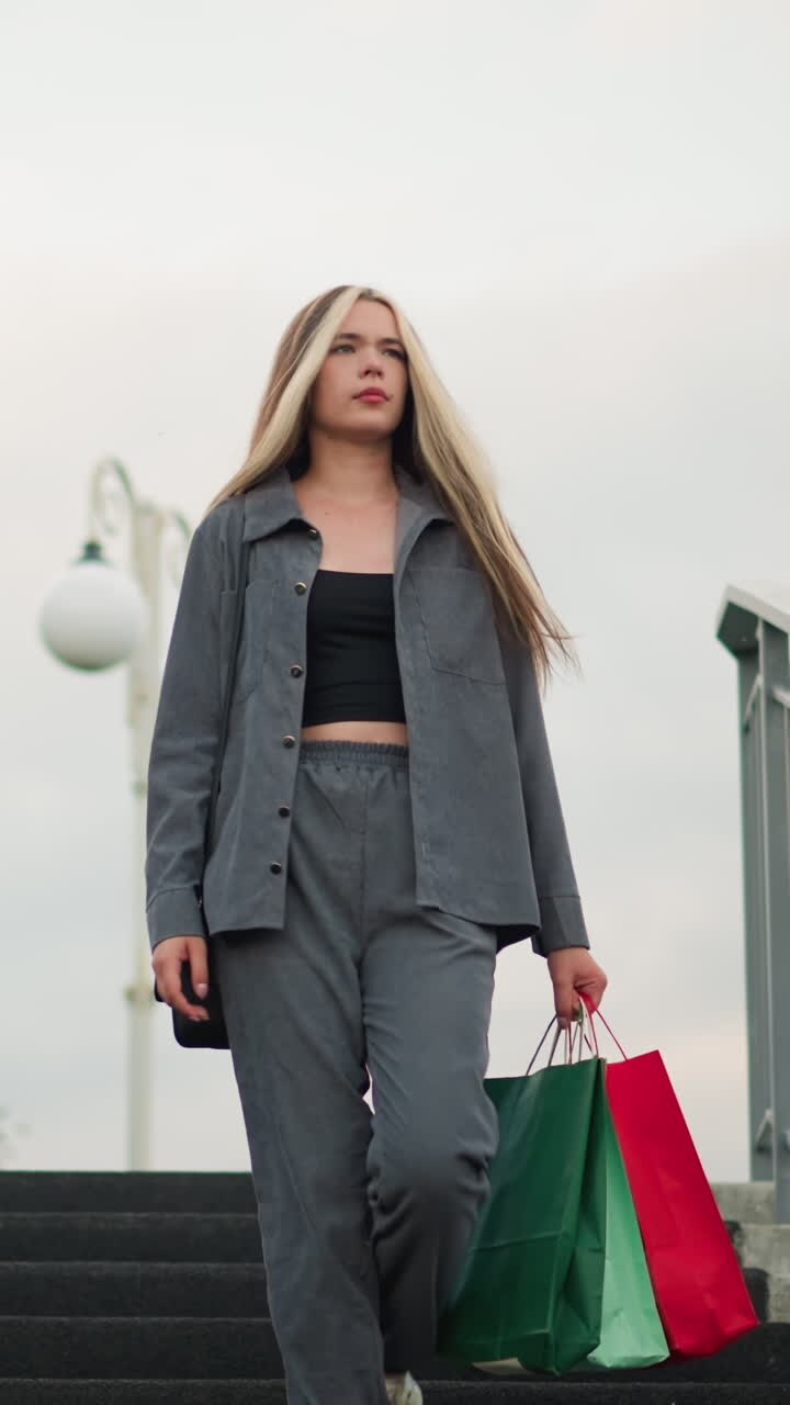 Lady carrying shopping bags walking down stairs while glancing at her steps, lamp post visible in the background with iron railings on both sides of the stairs