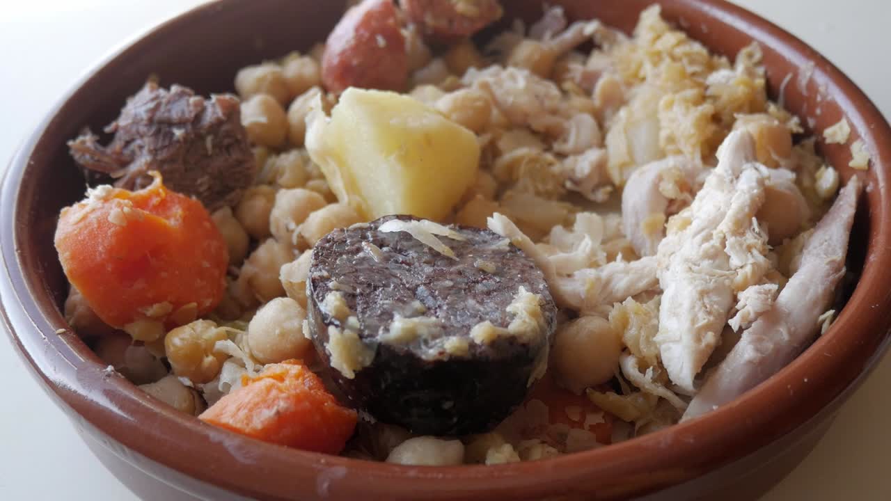 Traditional cocido stew in a clay bowl on a light background