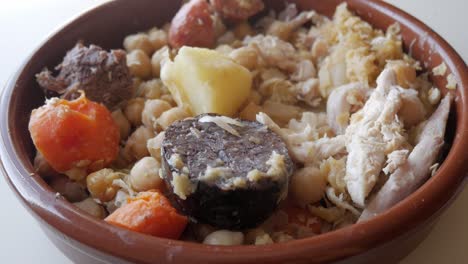 traditional cocido stew in a clay bowl on a light background