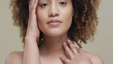 mujer biracial con cabello oscuro tocando la cara sobre un fondo beige, cámara lenta
