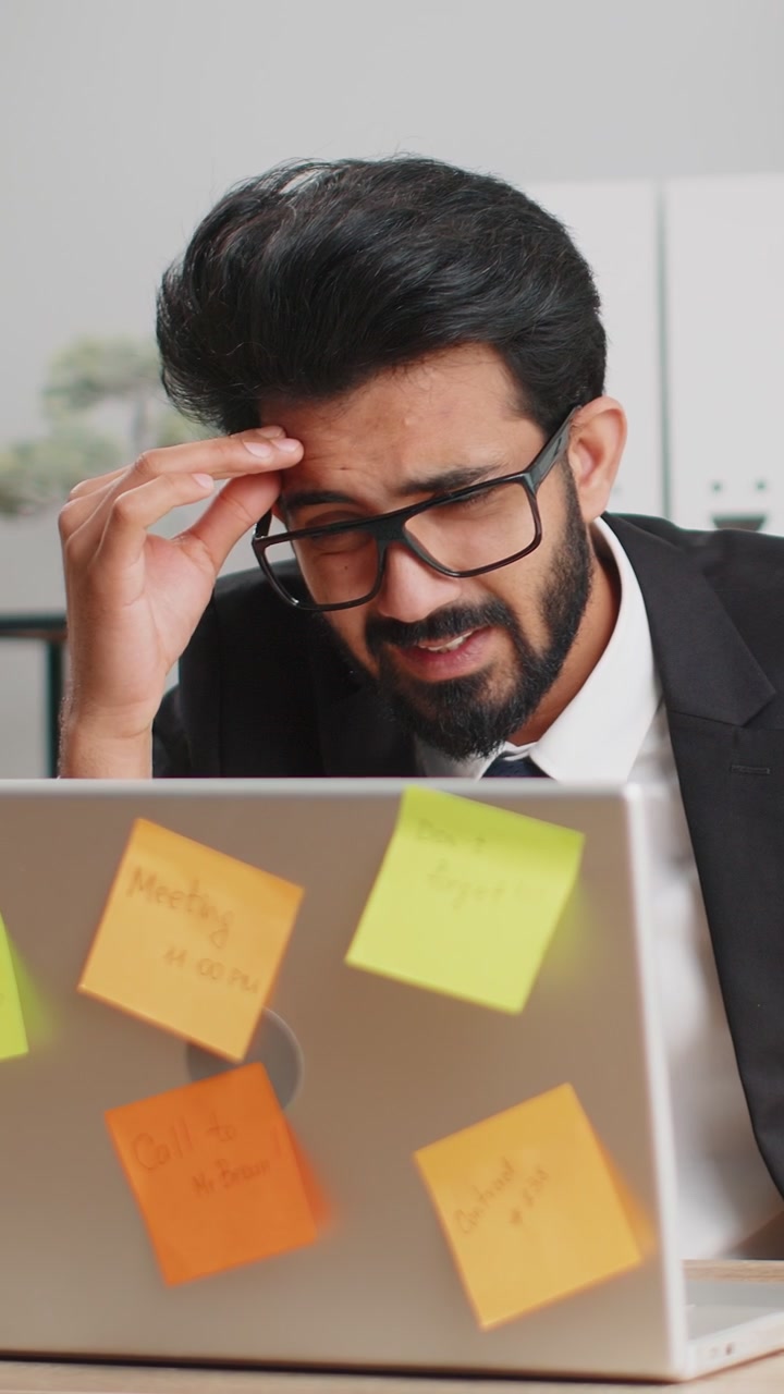 Tired sad exhausted businessman working on laptop at office with many sticker tasks panic attack