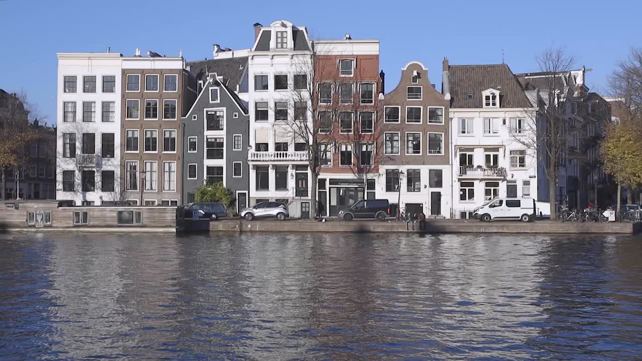 네덜란드 암스테르담의 전형적인 운하 주택은 푸른 하늘이 있는 화창한 날 앞에 있는 운하에 반사되어 있습니다.