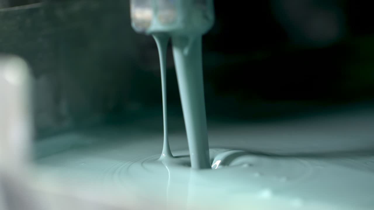 Extreme closeup of pale green paint endlessly pouring out of a valve