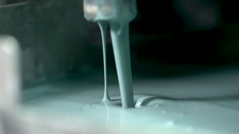 extreme closeup of pale green paint endlessly pouring out of a valve