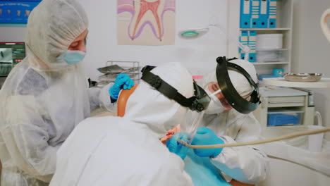 orthodontist doctor in protection suit drilling kid tooth in dental clinic