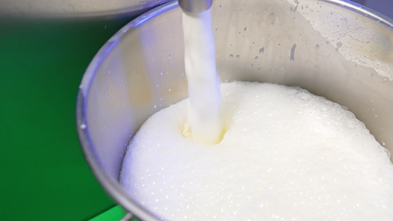 Fresh milk is pouring into a metal bucket creating foam on top. Close up. Food factory production concept.