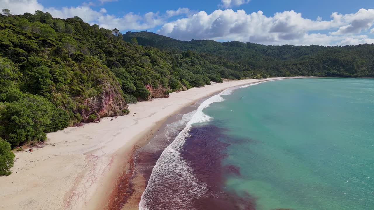 Un drone 4K cattura New Chums Beach, una spiaggia di sabbia bianca incontaminata nell’Isola del Nord della Nuova Zelanda. Le acque calme, la vegetazione lussureggiante e le ampie vedute costiere creano una scena serena