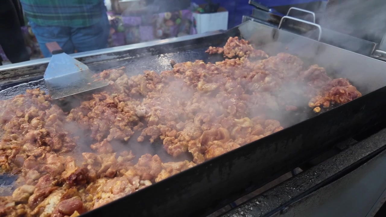 Pollo fresco condito cuoce su una piastra calda presso un affollato chiosco di taco da strada mentre il vapore sale, catturando l'autentica preparazione di cibo da strada e la cultura culinaria all'aperto.