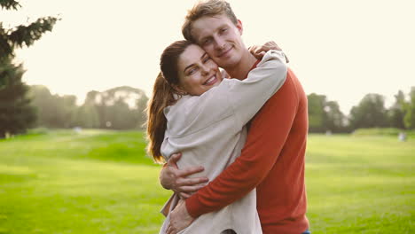 pareja feliz sonriendo a la cámara y abrazándose en el parque