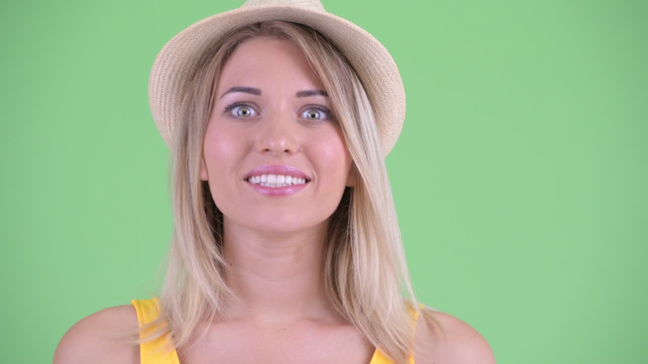 Studio shot of young tourist woman making funny faces against green background