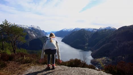 young woman arrives scenic viewpoint and sit down to enjoy fjord and mountain view, veafjord norway