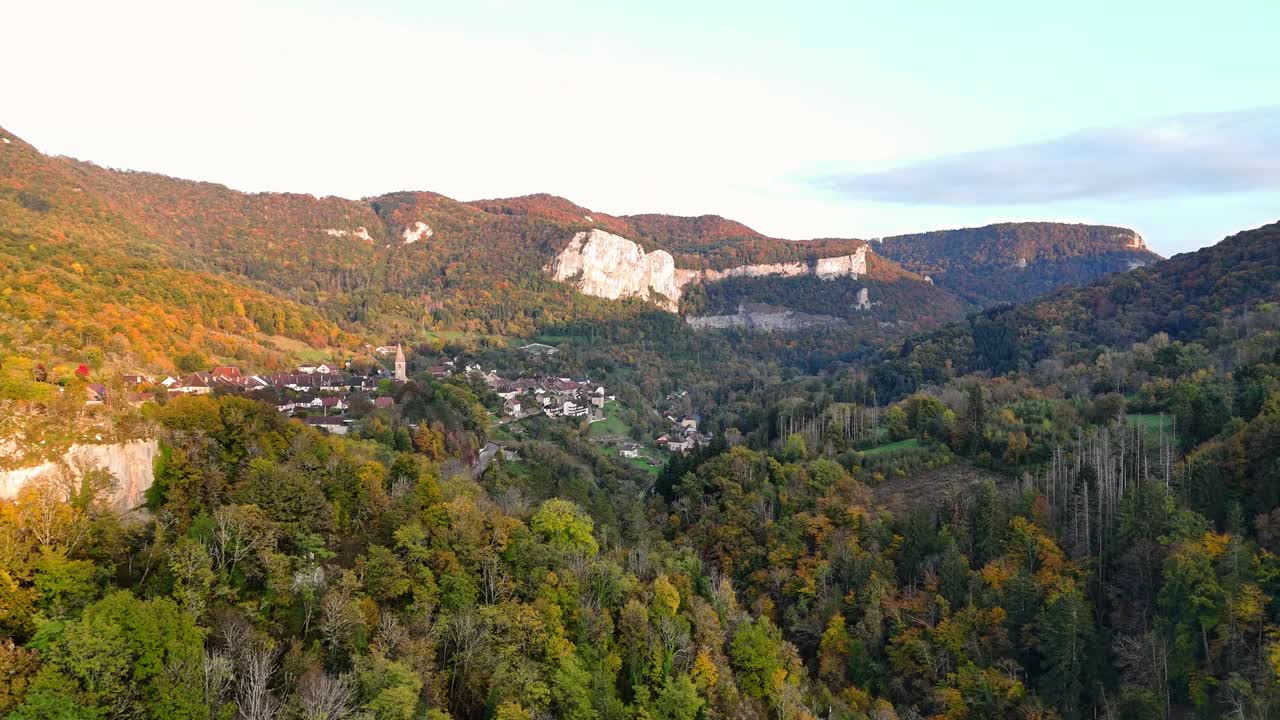 Aerial drone shot glides slowly above the wooded valley and village of Mouthier‑Haute‑Pierre in the Doubs department, Bourgogne‑Franche‑Comté region of eastern France